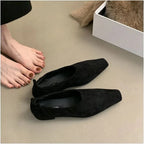 Une paire de ballerines noires au sol, un pied nu à côté