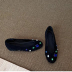 deux ballerines noires posées sur un tapis avec pierres décoratives bien visibles