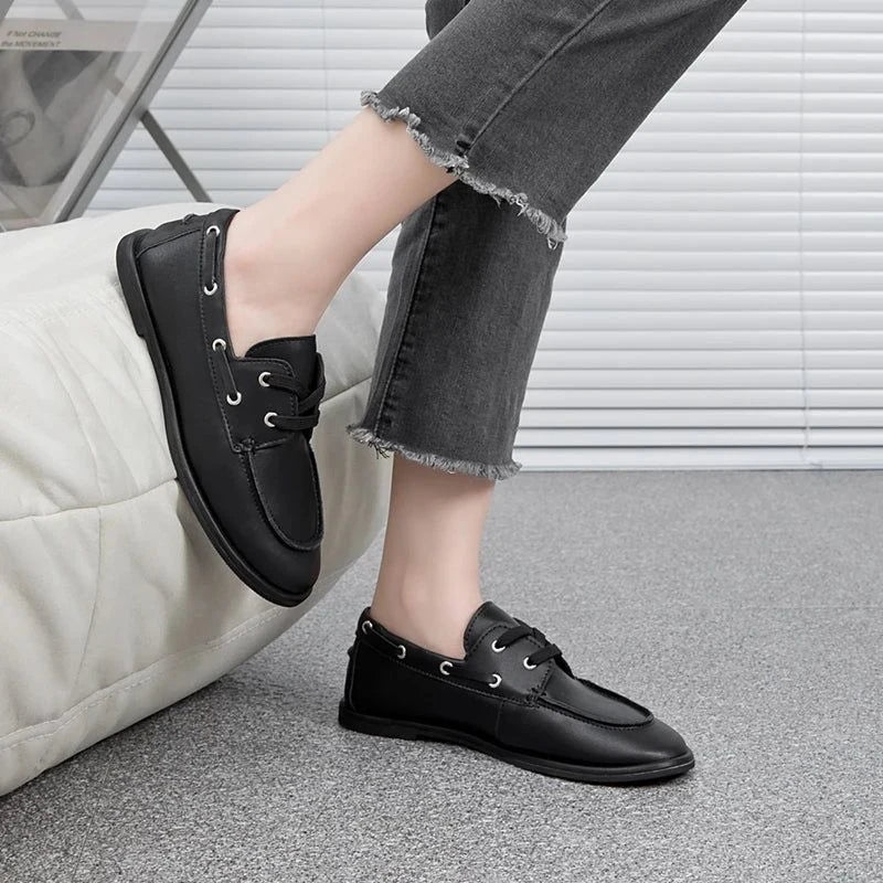 zoom sur une chaussure noire portée, jambe pliée près d’un pouf blanc