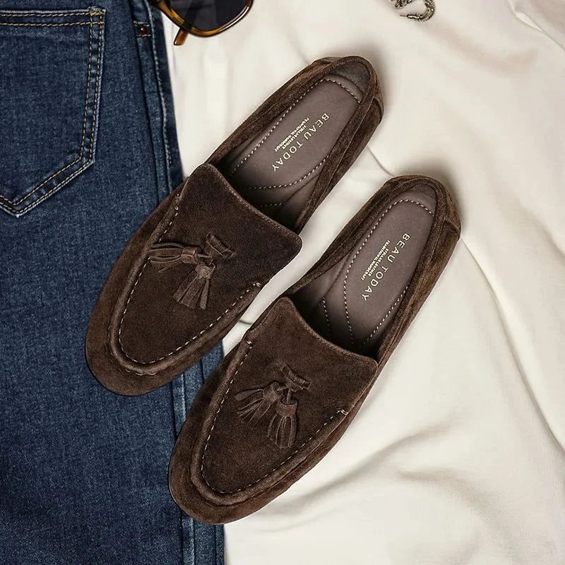Paire de mocassins en daim marron posée près d’un jean sur une surface claire