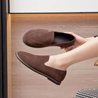 chaussures marron portées, l'une tenue à la main, jambes croisées
