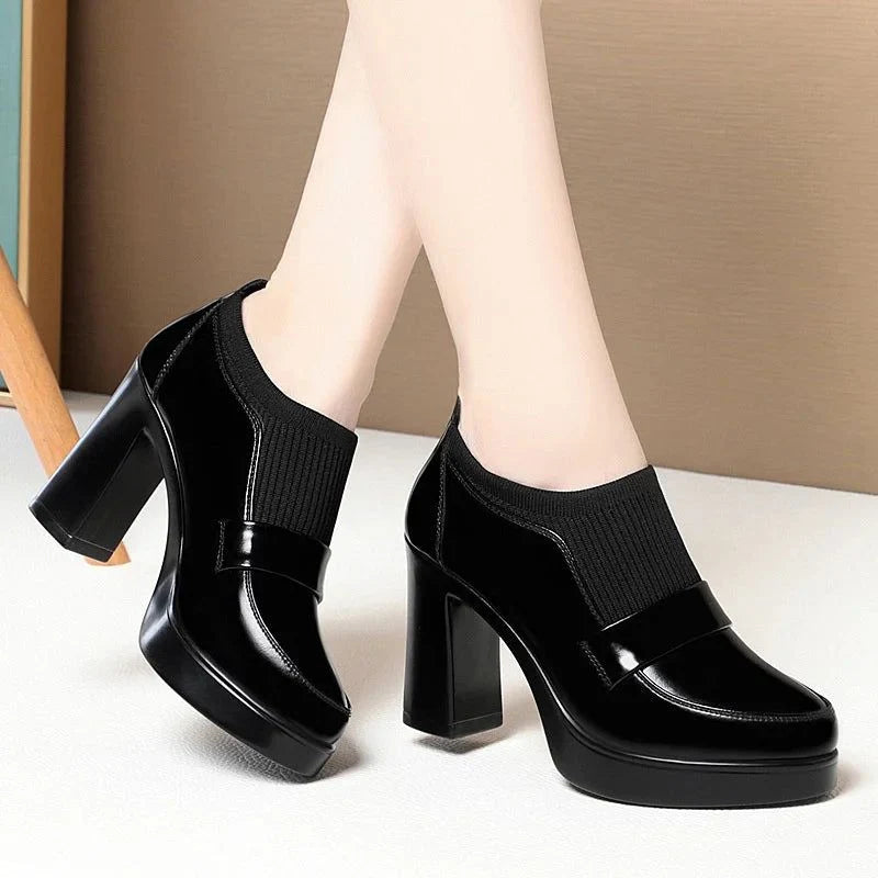 mocassins noirs à talon haut portés, jambes croisées sur fond neutre