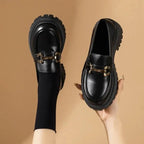 Mocassins vernis noirs portés avec des chaussettes noires, tenus en main et portés