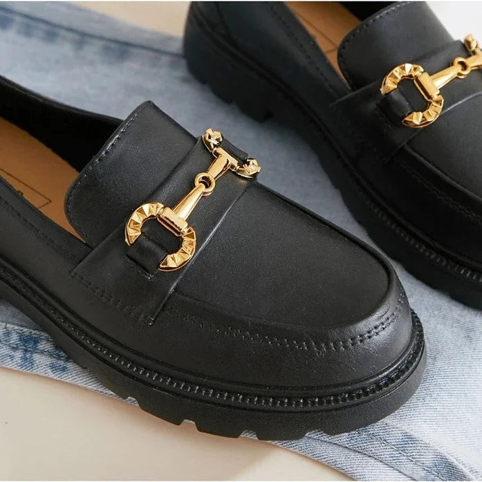 Gros plan sur la boucle dorée et le dessus du mocassin noir