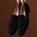 deux mocassins noirs tenus à la main devant un fond marron