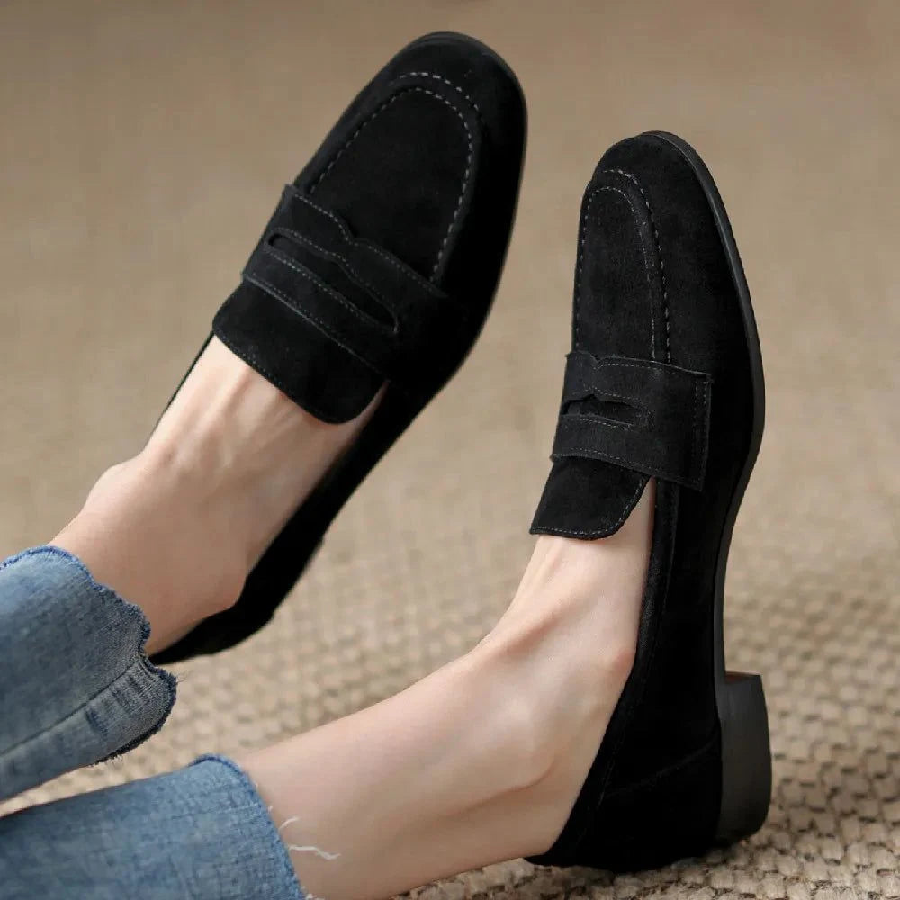 paire de mocassins noirs portée, jambes croisées sur tapis