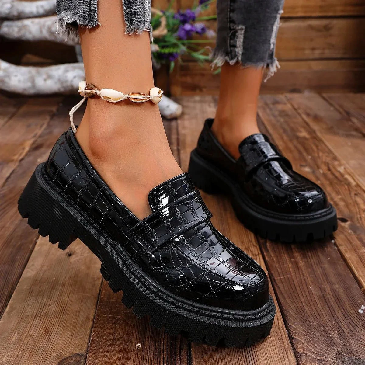 paire de mocassins vernis noirs portée avec un jean effiloché et bracelet cheville coquillage