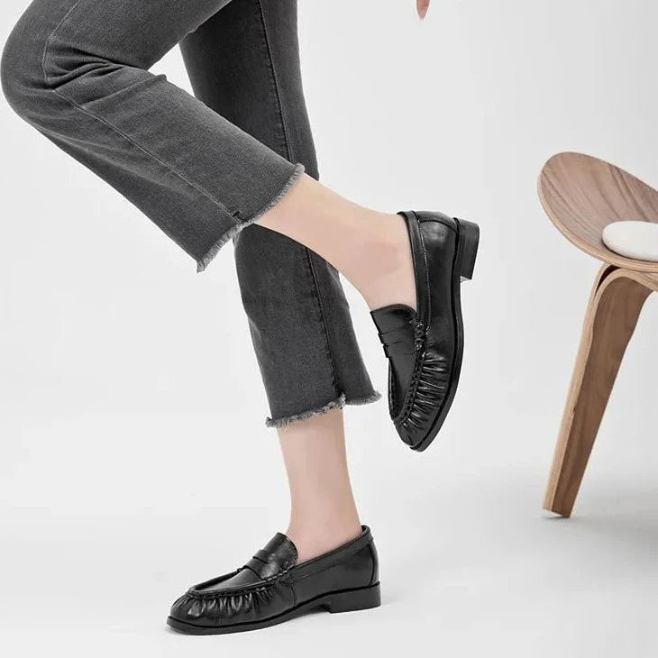 mocassins noirs portés avec la jambe croisée devant une chaise moderne