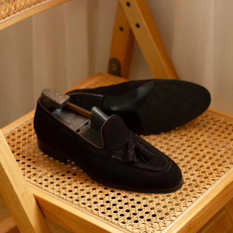 mocassin en daim foncé vu de côté sur une assise tressée, embauchoir à l'intérieur