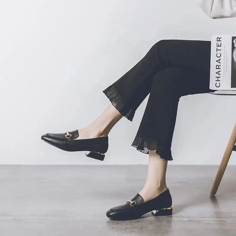 Vue de profil du mocassin noir porté avec un pantalon ample assise sur une chaise