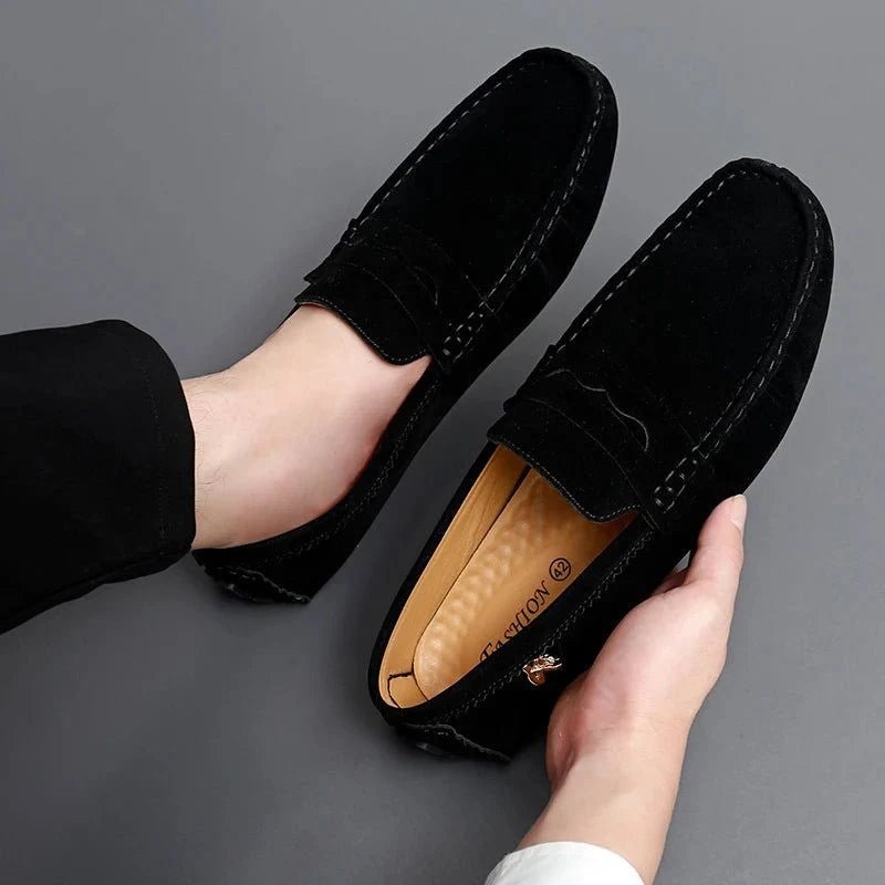 un mocassin noir enfilé, l’autre tenu à la main, fond gris