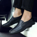 Mocassins noirs en cuir portés avec un pantalon noir, pied au sol près d'un véhicule