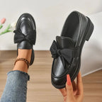 mocassin noir vu de dessus tenu à la main devant un décor minimaliste