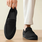 mocassin noir porté avec un pantalon clair, main tenant l’autre chaussure