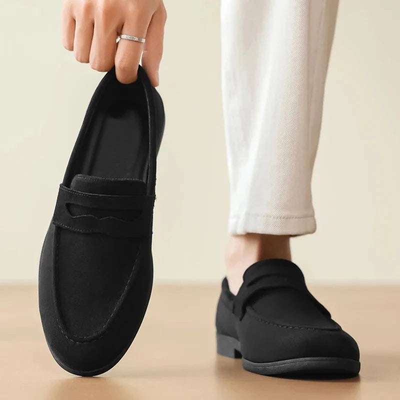 mocassin noir porté avec un pantalon clair, main tenant l’autre chaussure