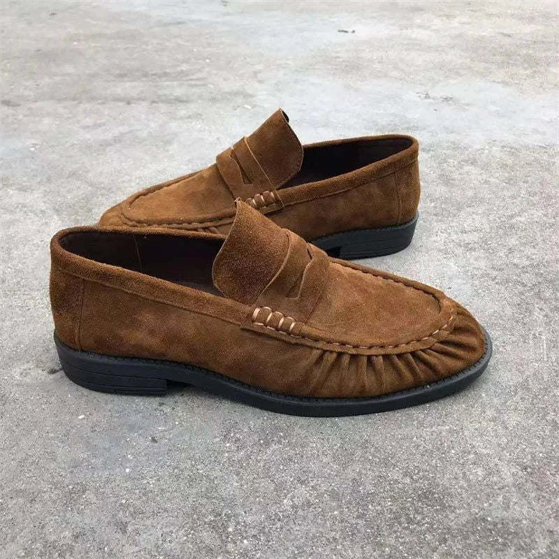 Vue de trois quarts des mocassins en suédine marron posés sur sol gris