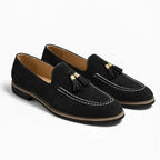 paire de mocassins noirs à glands posée sur fond uni, vue de trois quarts
