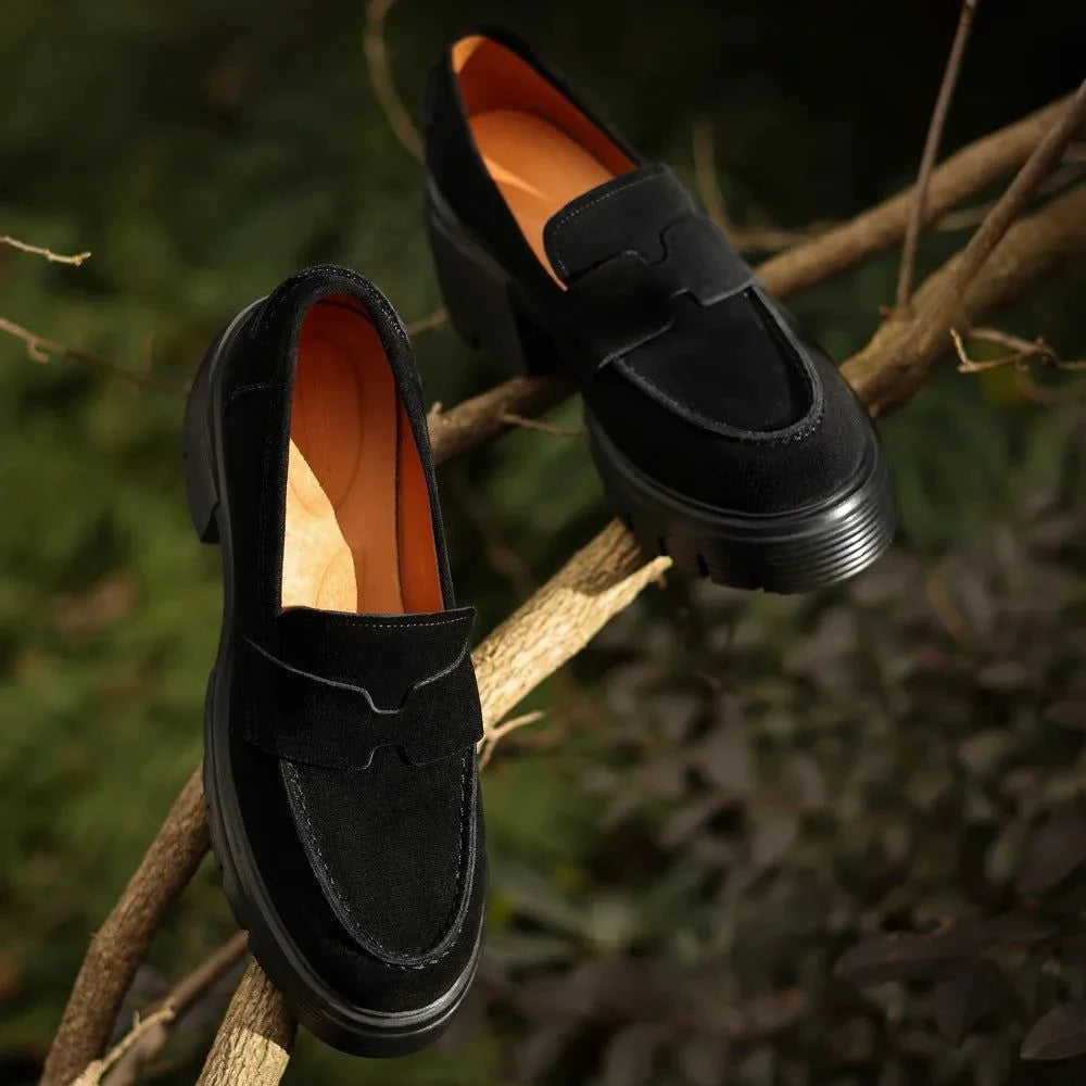 Deux mocassins noirs à talon épais posés sur des branches en extérieur