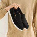 paire de mocassins noirs tenue à la main devant un pull beige