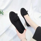 main tenant un mocassin noir, l’autre chaussure portée, fond clair
