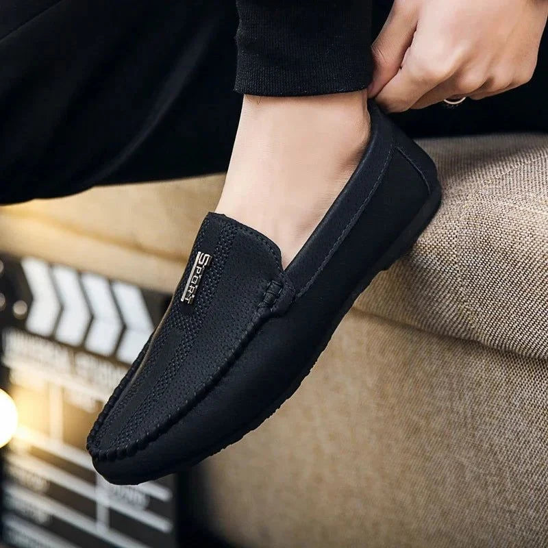 mocassin noir porté avec un pantalon foncé, pied sur un canapé clair