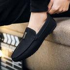 mocassin noir porté avec un pantalon foncé, pied sur un canapé clair