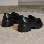 Paire de mocassins noirs à talons hauts vue de dos sur un tapis beige