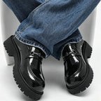 mocassins noirs vernis portés, pieds croisés sous une chaise, vue de face