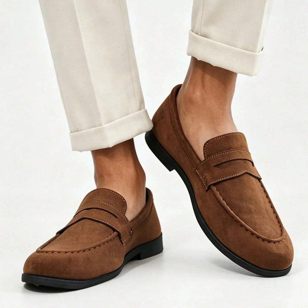 deux pieds chaussés de mocassins marron assortis à un pantalon crème