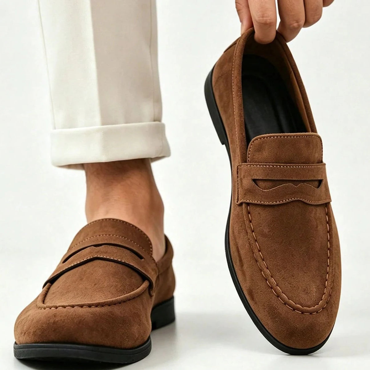chaussures marron portées avec un pantalon clair, une main tient l'une d'elles