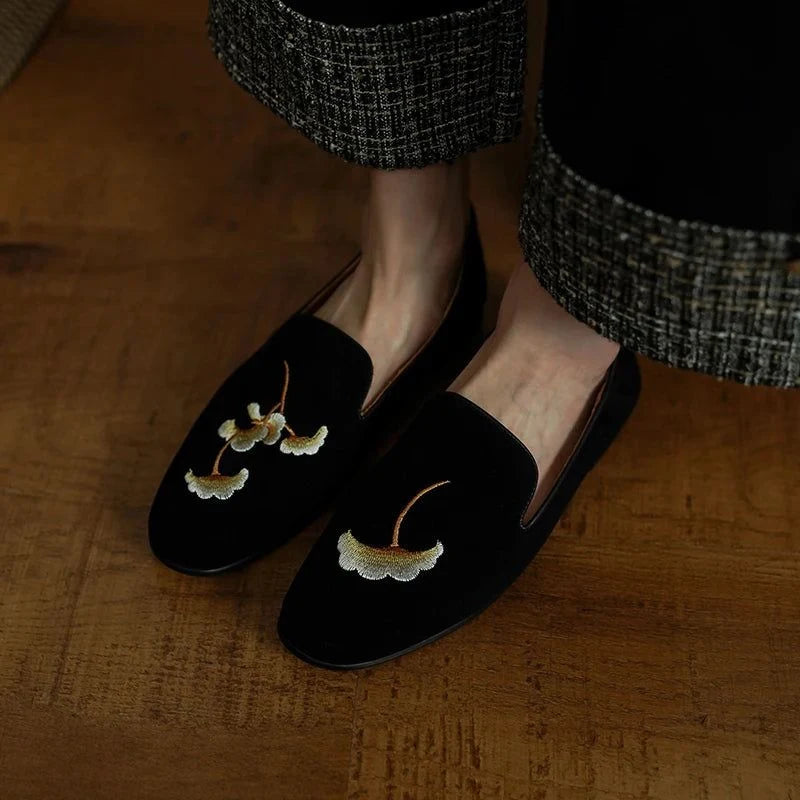 une paire de mocassins noirs brodés portée avec un pantalon à carreaux